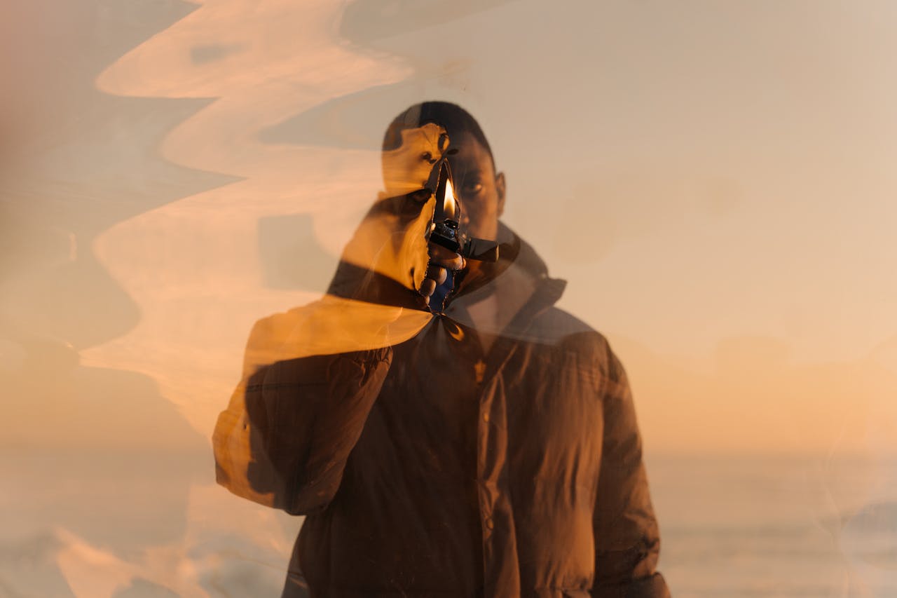A man holds a lit lighter behind a transparent plastic curtain at sunset, creating a warm and abstract effect.