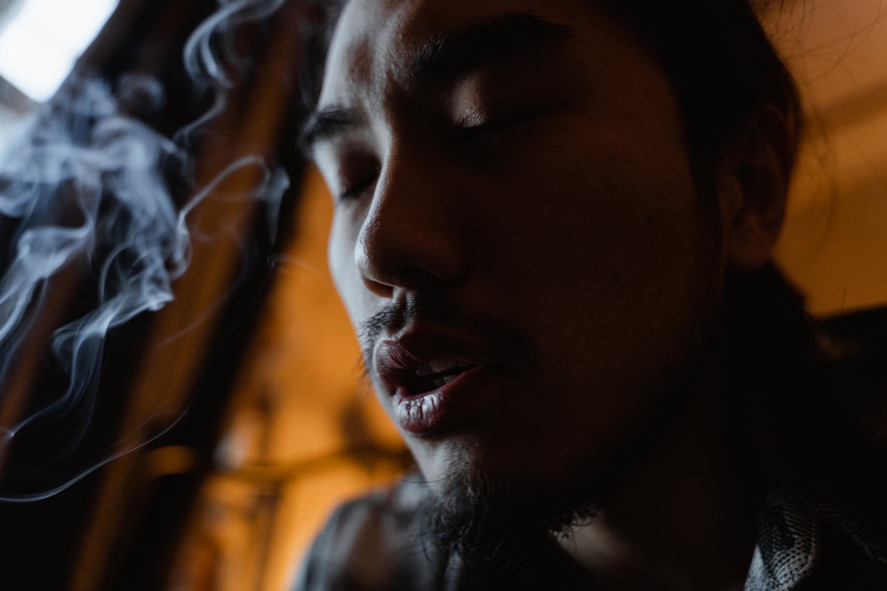 Close-up portrait of a young man with eyes closed, surrounded by smoke, in a contemplative mood.